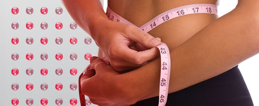 Close-up of a person measuring waist circumference against a backdrop of red light therapy bulbs, illustrating fat loss benefits.