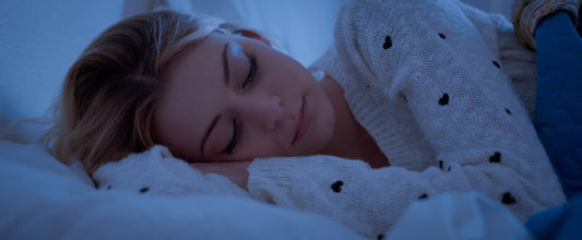 Woman sleeping peacefully in a dim blue light, illustrating the impact of blue light on sleep quality